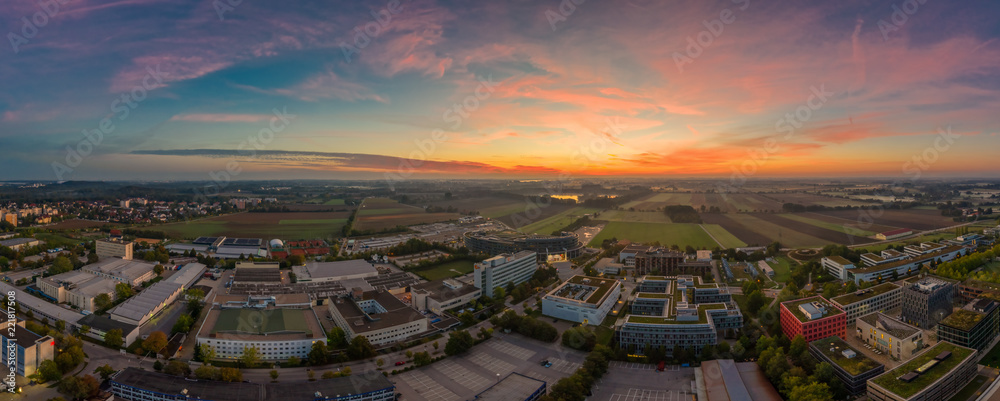 Sonnenaufgang in Bayern, Unterföhring im morgendlichen Glow zur aufgehenden Sonne mit einem Industriegebiet für Medien und einem See im Hintergrund