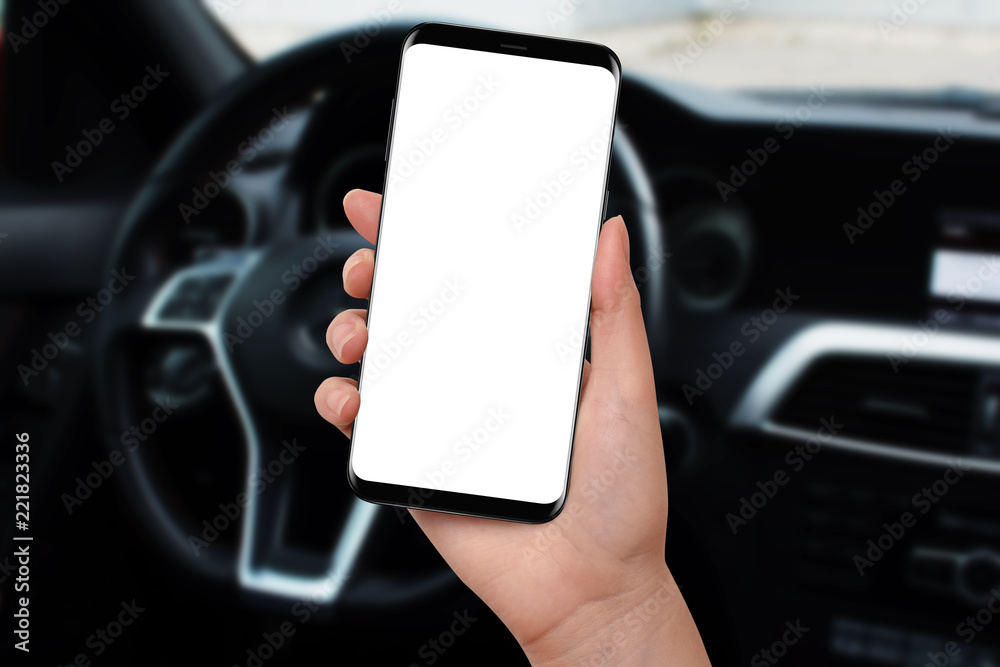 Female hand holding modern phone with isolated screen, steering wheel in background. Mockup