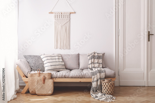 Beige wooden sofa and bags in white loft interior with decor on the wall next to door. Real photo
