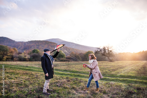 Carefree senior couple flying a kite in an autumn nature at sunset. photo