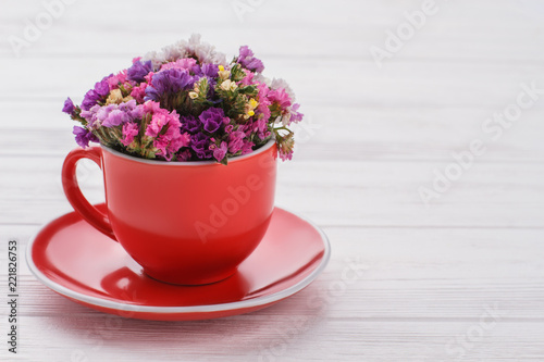 Limonium statice flowers bouquet in coffee mug. White wood background.