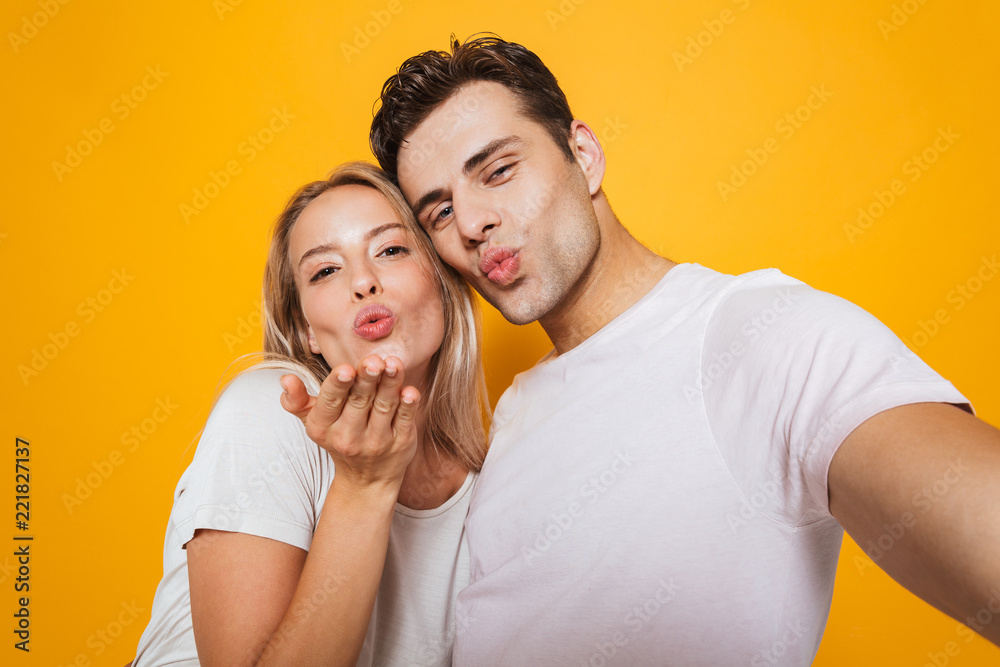 Naklejka premium Loving couple standing isolated over yellow wall background take a selfie by camera.