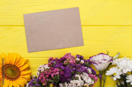 Bouquets of flowers and blank paper on yellow wood. Top view, flat lay.