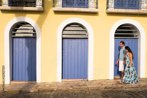 Couple on cobbled street with yellow wall and blue doors in a historic city.