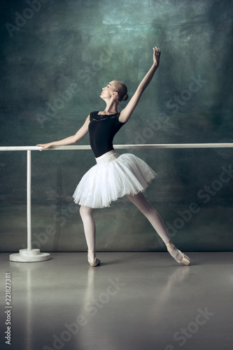 The classic ballet dancer in white tutu posing at ballet barre on studio background. Young teen before dancing. Ballerina project with caucasian model. The ballet, dance, art, contemporary