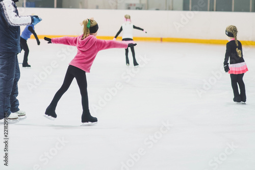 Little girls learning to ice skate. Figure skating school. Young figure skaters practicing at indoor skating rink.