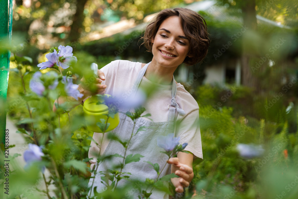 Woman gardener standing over plants in greenhouse water flowers Woman gardener standing over plants in greenhouse water flowers