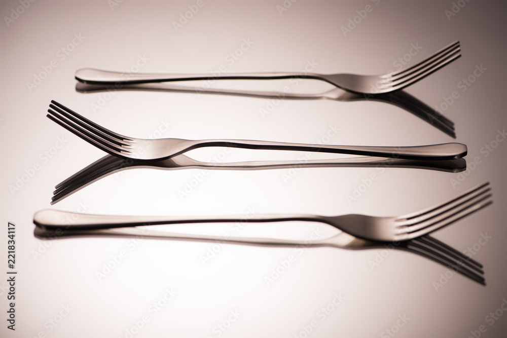 close-up view of three arranged shiny forks reflected on grey close-up view of three arranged shiny forks reflected on grey