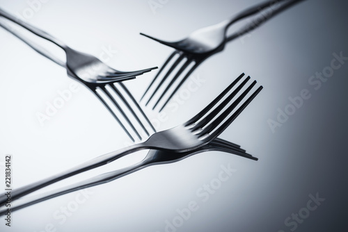 close-up view of three shiny forks reflected on grey