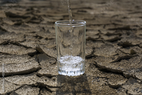 pure clear fresh water is poured into a glass beaker standing in the middle of a dry cracked clay desert land