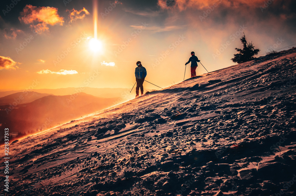 Obraz premium Couple silhouette in ski resort. Warm sunset in background. Skiing in two