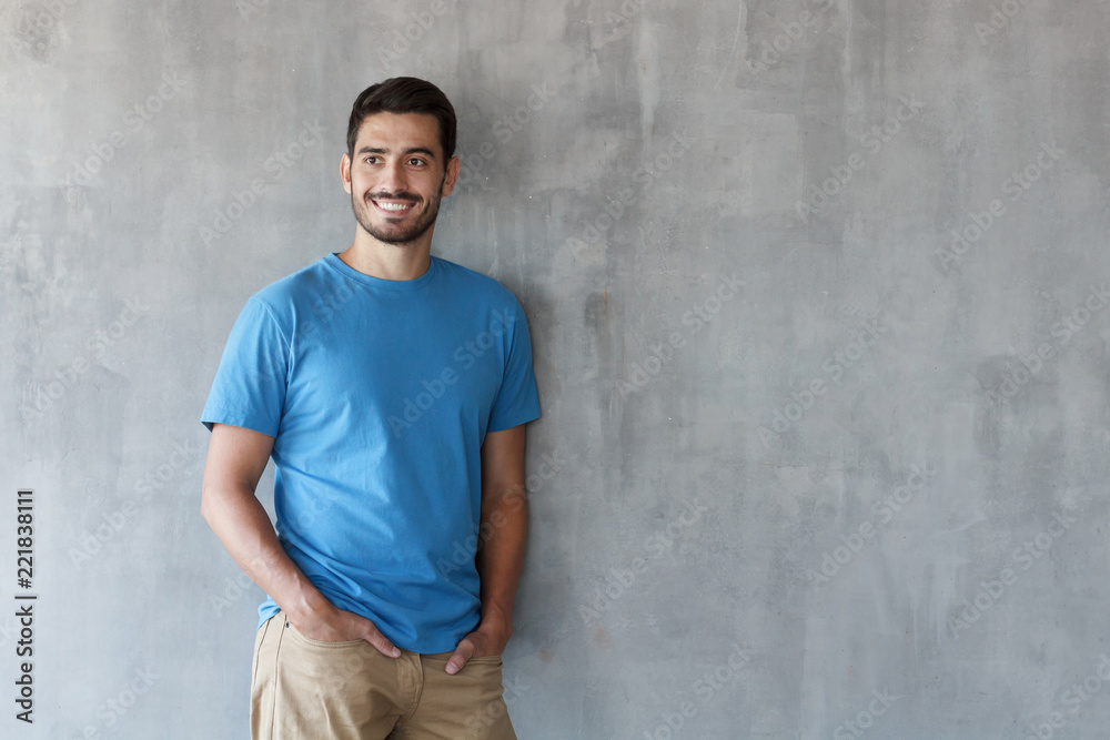 Horizontal shot of young handsome European Caucasian male isolated on grey background standing with back turned to wall so that there is copyspace on right for advertising goods, services or apps Horizontal shot of young handsome European Caucasian male isolated on grey background standing with back turned to wall so that there is copyspace on right for advertising goods, services or apps