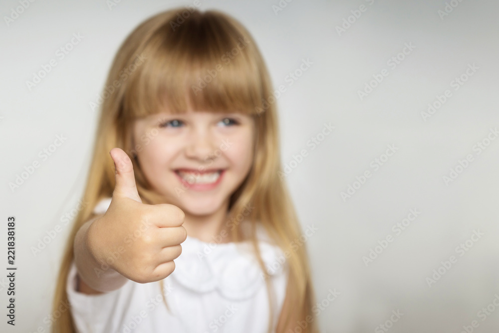 little blonde girl in white dress smiles and shows thumb up. focus on the finger. copy space little blonde girl in white dress smiles and shows thumb up. focus on the finger. copy space