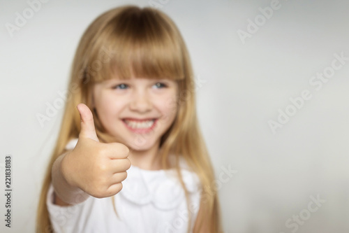 little blonde girl in white dress smiles and shows thumb up. focus on the finger. copy space