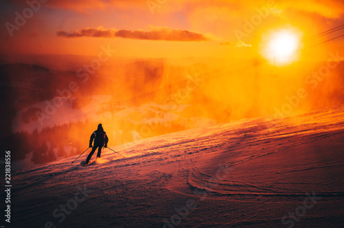 Fototapeta Naklejka Na Ścianę i Meble -  Man ski in ski resort. Winter sport photo. Orange sunset light in background. Edit space. Christmas and New Year time, snowy photo, edit space