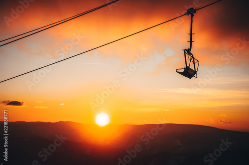 Ski lift silhouette in ski resort, winter sunset in background.
