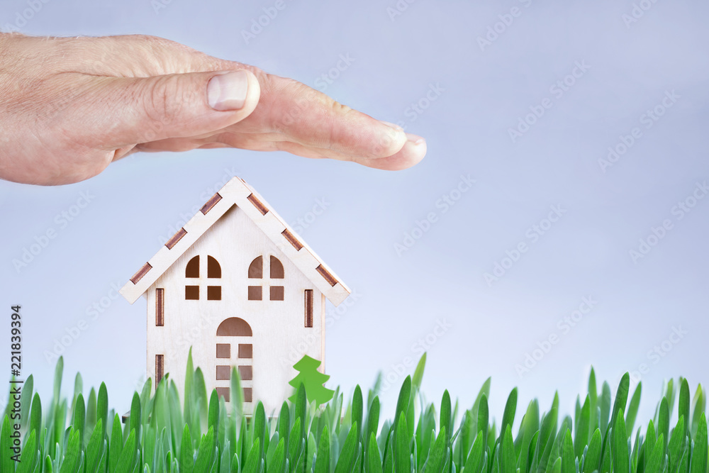 Hand protecting a model house on the green lawn with copy space, real estate or insurance concept Hand protecting a model house on the green lawn with copy space, real estate or insurance concept