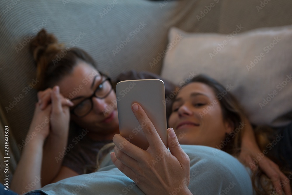Lesbian couple using mobile phone on sofa Lesbian couple using mobile phone on sofa
