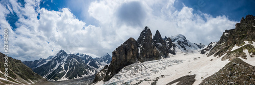 Summer mountain panorama in Western Caucasus. Ahsu glacier, snow covered mountains near Ushba and rocks against stormy sky.