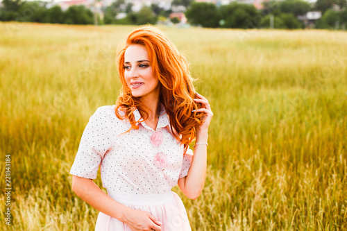 Portrait of a young red-haired woman in a tall yellow grass at sunset.