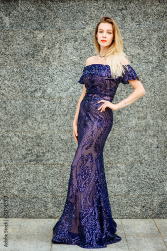 Fashionable portrait of style. Young beautiful woman in a blue long dress posing on the stairs against the old city building.The girl is outdoors
