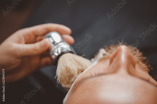 Barber process shaving razor bearded hipster man in barbershop.