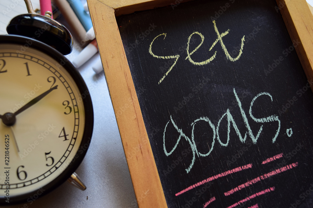 Set goals on phrase colorful handwritten on chalkboard, alarm clock with motivation and education concepts Set goals on phrase colorful handwritten on chalkboard, alarm clock with motivation and education concepts