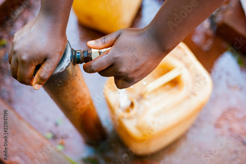 above close view up of young african child hand filling tank with tap water with green background