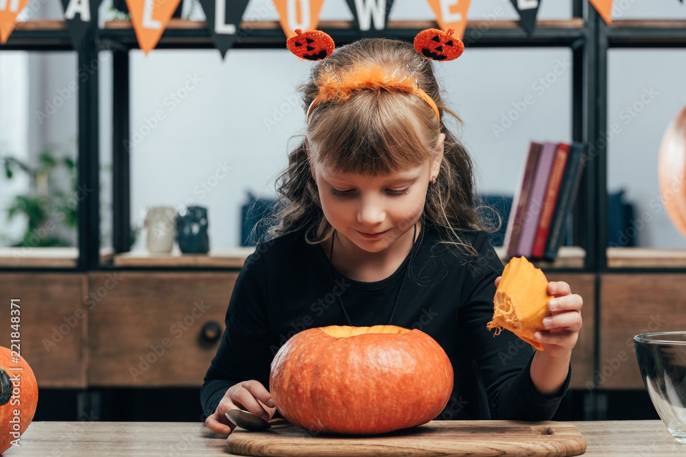 Fototapeta premium portrait of adorable child at tabletop with pumpkin for halloween at home