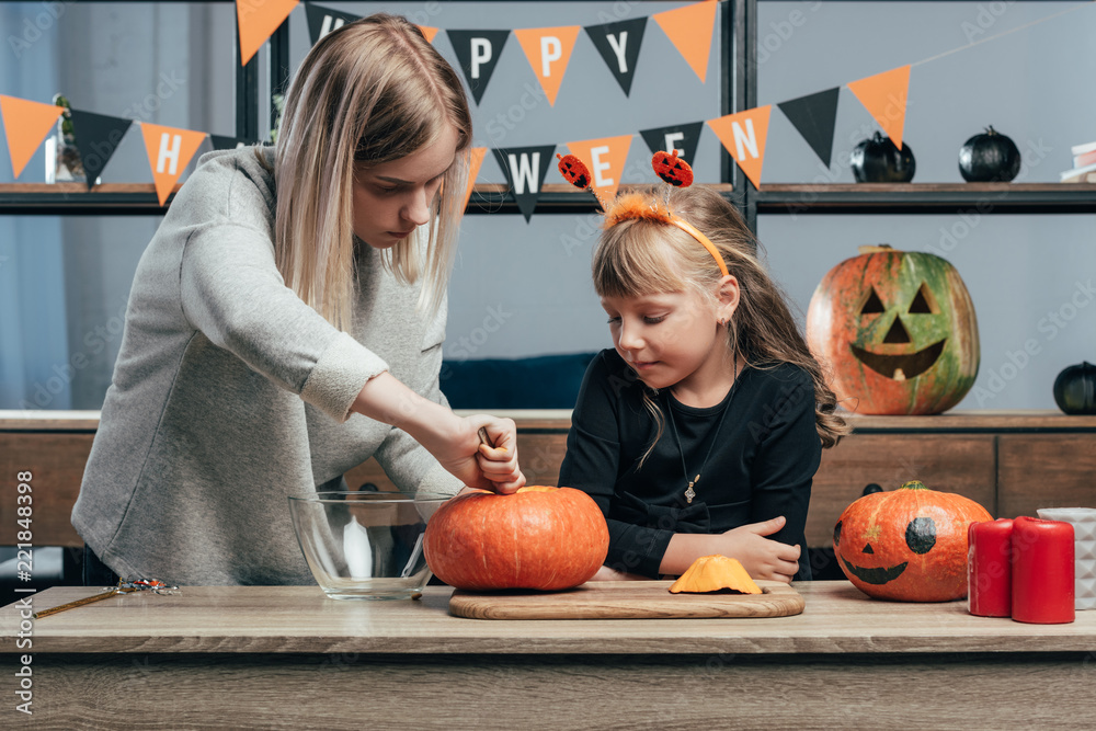 Fototapeta premium young woman helping little sister in halloween costume carving pumpkins at home