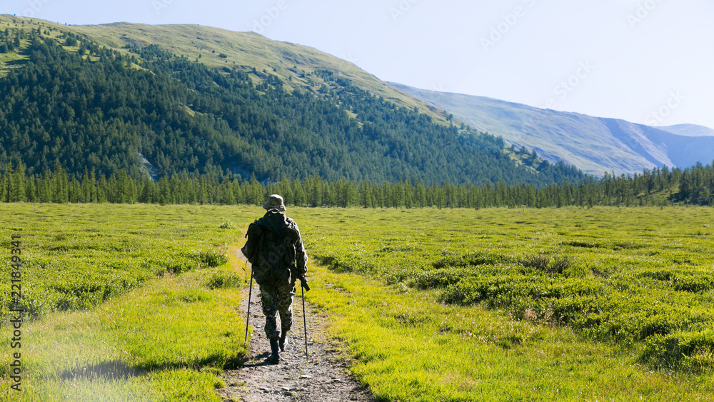 A tourist in a hike in the mountains. A man with a backpack on his shoulders travels alone through the mountains of Russia.