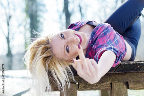 Blonde girl laying on table in nature with middle finger up on hand