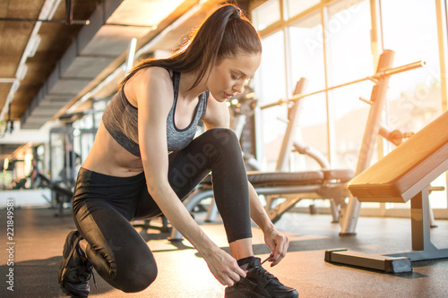 Young fit woman tying her shoelaces at gym