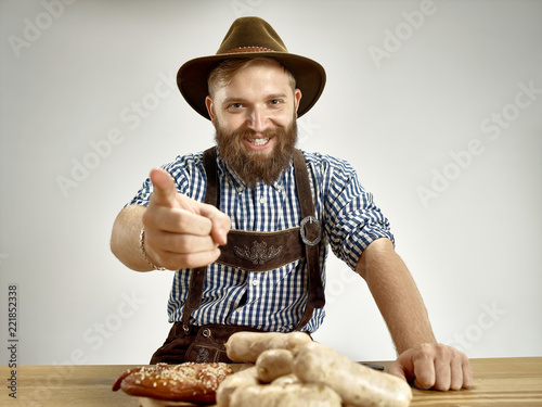 Germany, Bavaria, Upper Bavaria. The young smiling man with beer dressed in traditional Austrian or Bavarian costume in hat sitting at table at studio