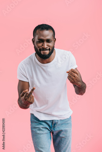 portrait of young afircan american man showing middle fingers isolated on pink photo