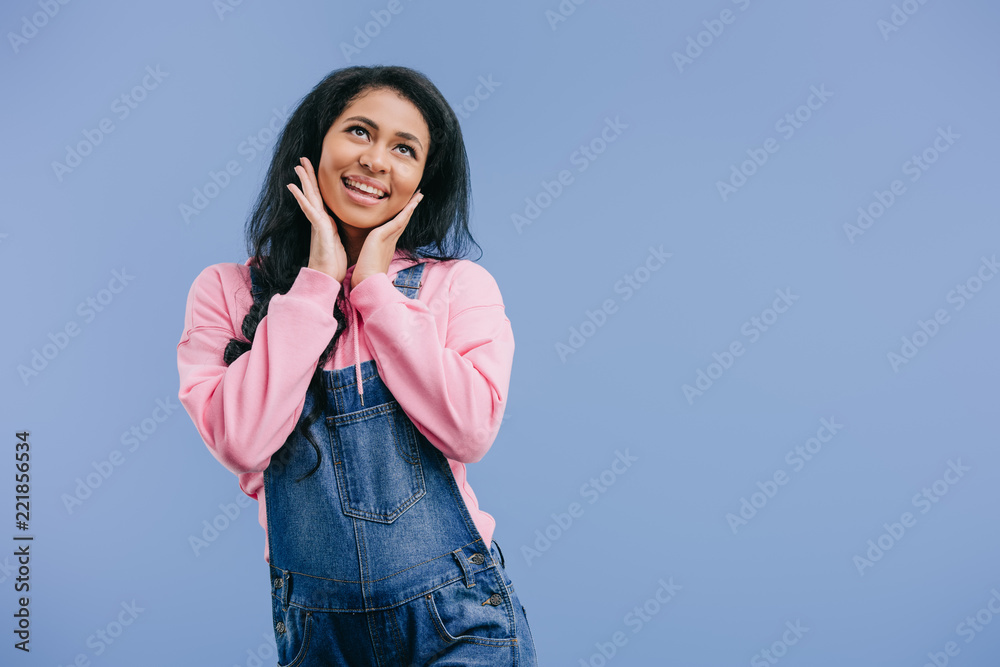 dreamy young african american woman with hands on cheeks isolated on blue background dreamy young african american woman with hands on cheeks isolated on blue background