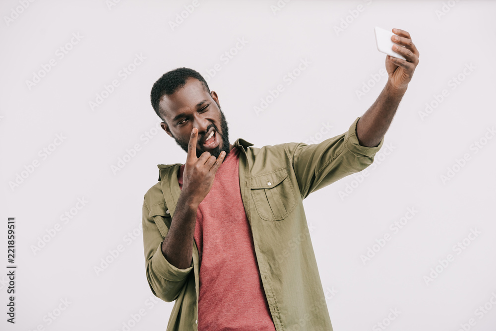 smiling handsome african american man taking selfie with smartphone and showing rock sign isolated on white smiling handsome african american man taking selfie with smartphone and showing rock sign isolated on white