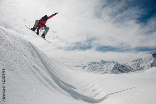 guy is jumping on a snowboard against a blue sky and snow-capped mountain peaks