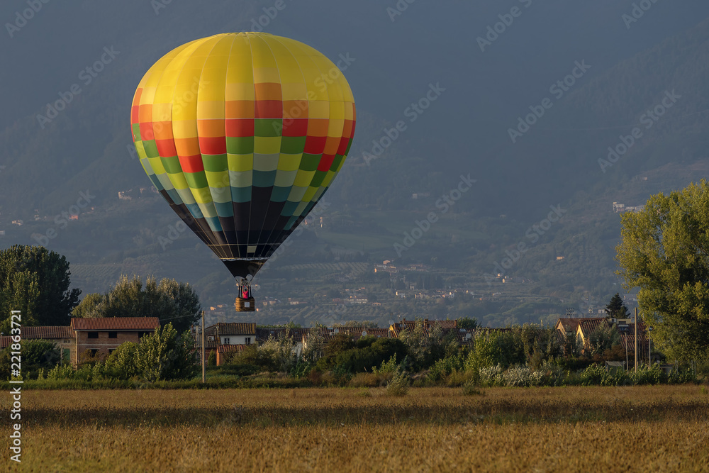 Obraz premium Colorful hot-air balloon flies over typical village in the Tuscan countryside in the light of the sunset