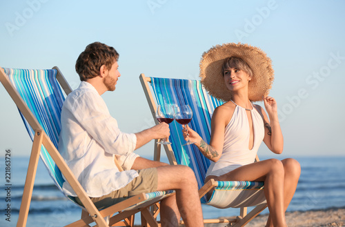 Young couple with glasses of wine in beach chairs at seacoast