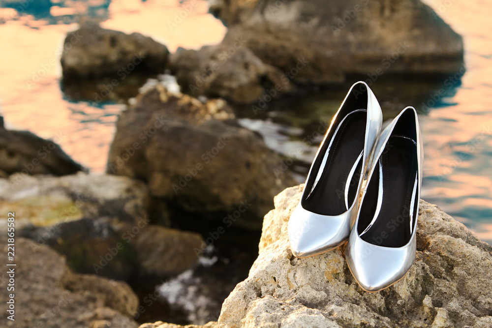 Close-up shot of Pair of Silver High Heel Shoes on yellow stones near sea Close-up shot of Pair of Silver High Heel Shoes on yellow stones near sea