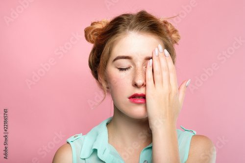 young woman with eyes closed covering half of her face with a palm of her hand. pretty girl portrait on pink background.