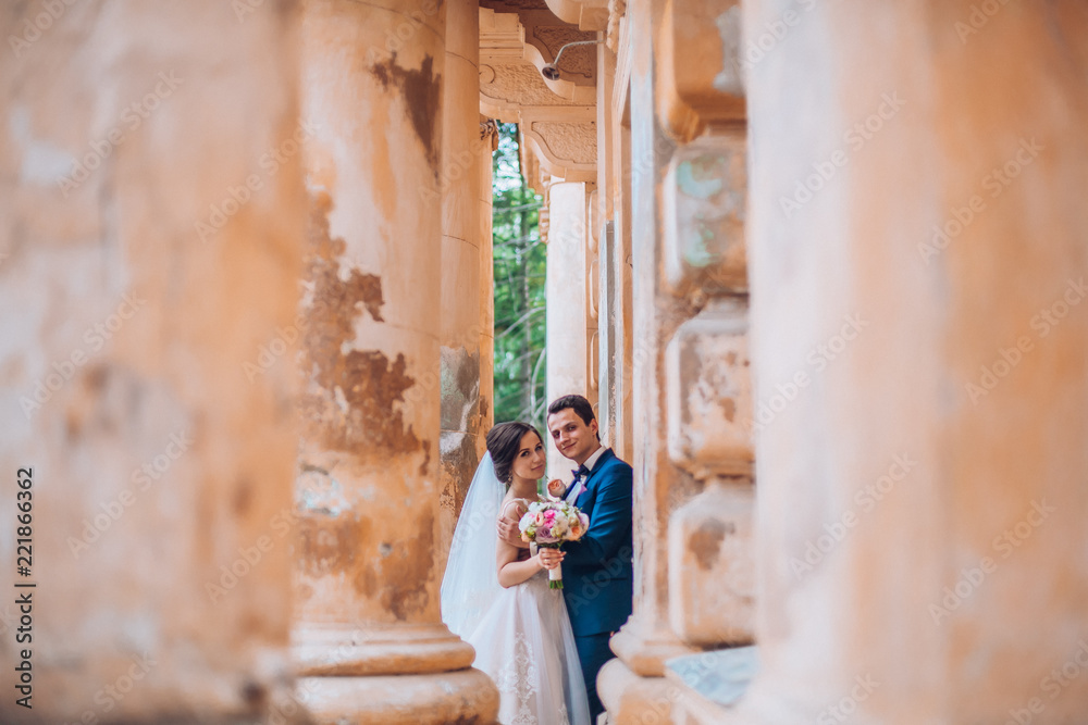 Sensual wedding married couple, valentines hugging in front of old slavic castle. Wedding day of bride and groom. Man and woman posing near old columns. Wedding photoshoot.