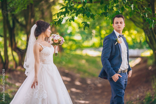 Romantic wedding moment, couple of newlyweds smiling portrait, bride and groom hug while on a walk in the park. Wedding day in green trees tunel.