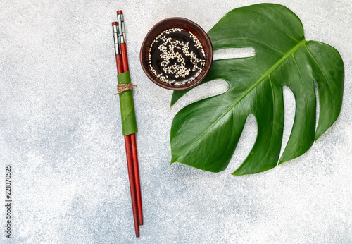 Asian food concept.  soy sauce with white sesame and Chopstick on a gray concrete surface with tropical leaves
