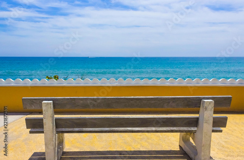 Empty bench on a wooden deck at the shore of beautiful blue sea in a hot sunny day