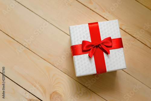 Gift box with red ribbon on wooden background.
