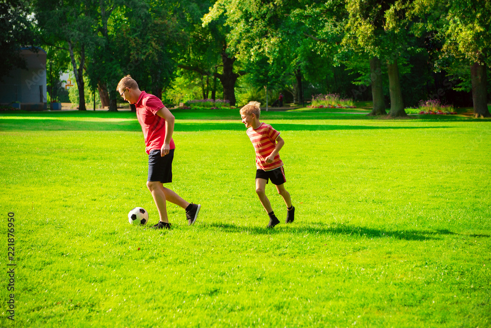 Happy young father play with his little son football in sunny park
