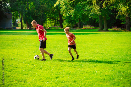 Happy young father play with his little son football in sunny park