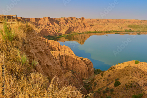 Spectacular red mountain landscape with viewpoint towards a calm lake and vegetation in the background in the Barrancas de Burujon, Toledo, Spain